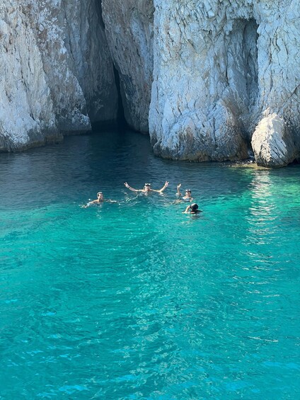 People swimming in clear turquoise water with rocky cliffs in the background. 2