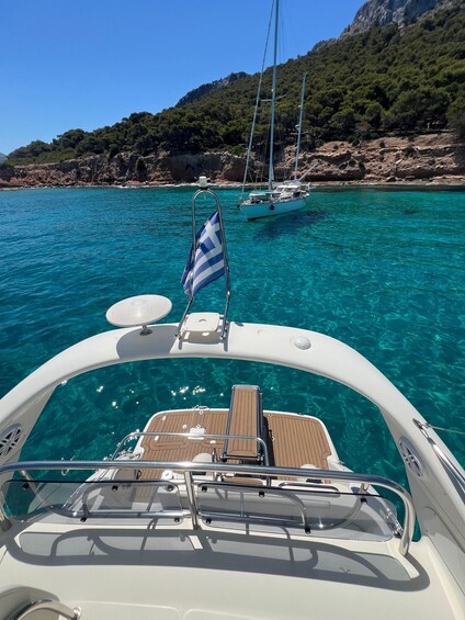 A boat on clear turquoise water with a flag, a rocky coastline, and a sailboat in the distance. 3