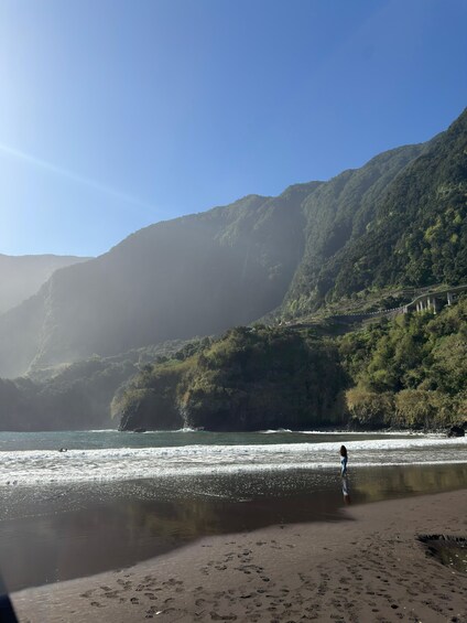 A beach with footprints, a person walking, and a mountain in the background. 1