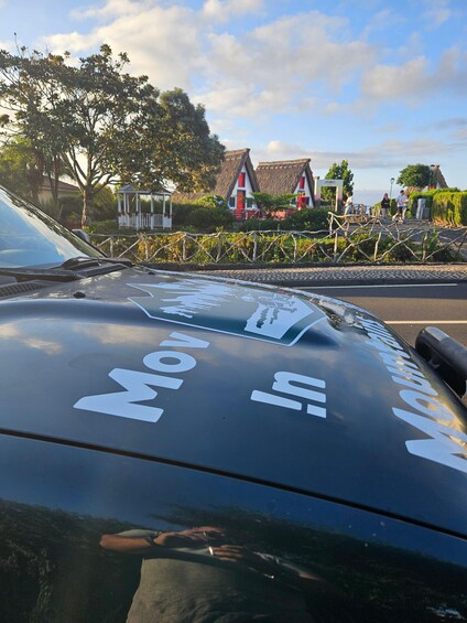 A car with 'Movin In' decals, a thatched-roof house, and a clear sky. 1