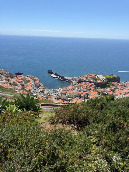 A coastal town with red-roofed buildings, a rocky coastline, and a clear blue sky. 4