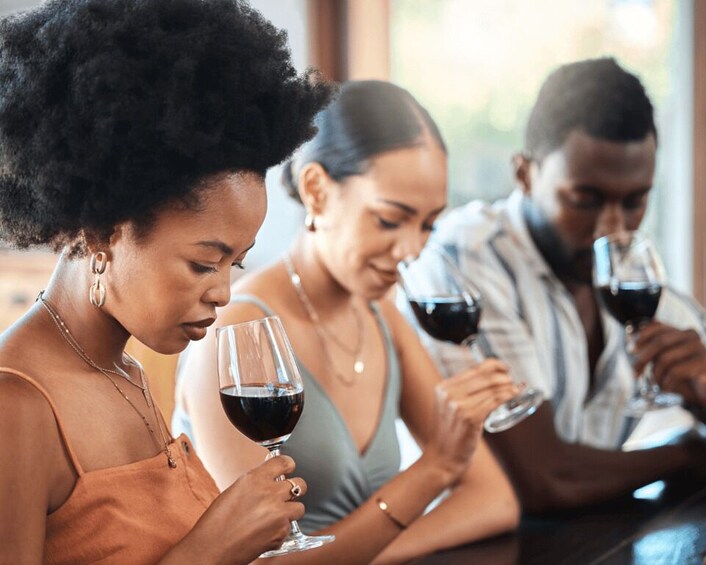 Three people sitting at a table, each holding a glass of red wine. 3