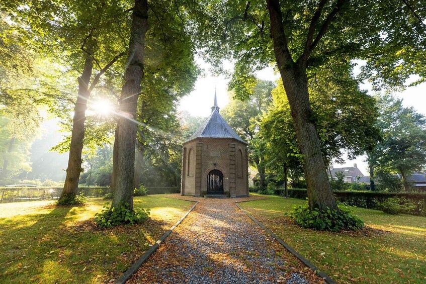 A brick structure with a pointed roof, surrounded by trees and a gravel path. 4