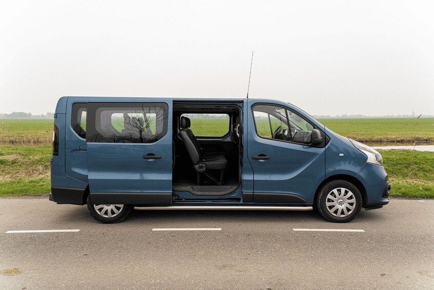 A blue van parked on a road with open doors, surrounded by open fields. 2