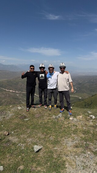 Four people standing on a grassy hill with a mountainous landscape in the background. 4