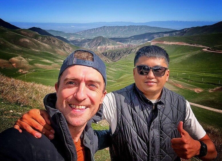 Two people taking a selfie with a mountainous landscape in the background. 1