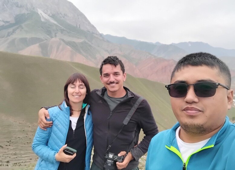 Three people standing in a mountainous landscape with a camera and a phone. 2