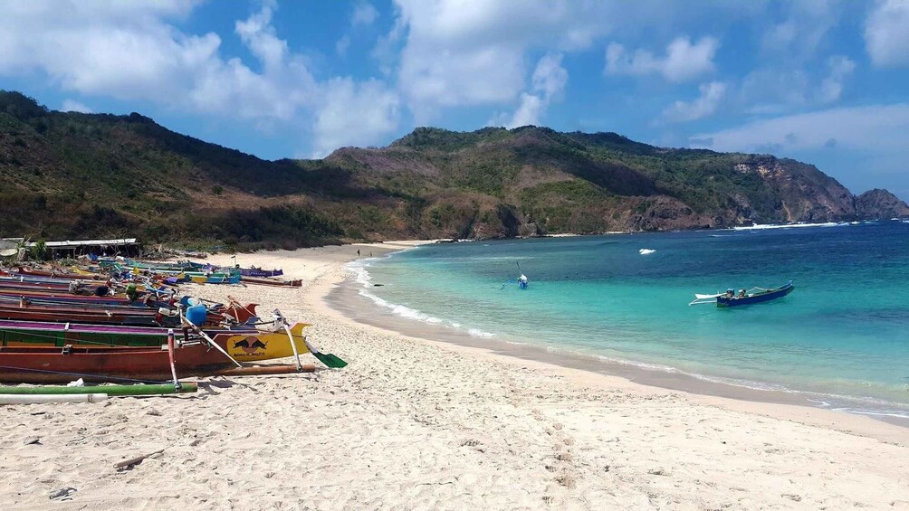 A beach with boats, clear turquoise water, and mountains in the background. 3