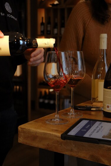 A person pouring red wine into two glasses on a wooden counter. 4