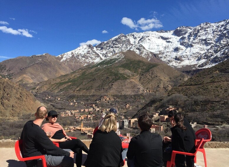A group of people seated on red chairs overlooking a village and snow-capped mountains. 5