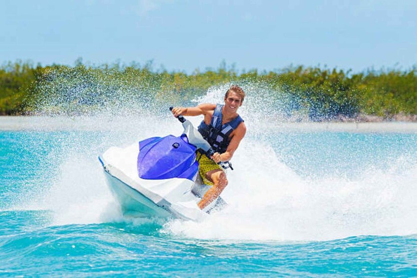 A person jet skiing on clear turquoise water with a tropical backdrop. 4