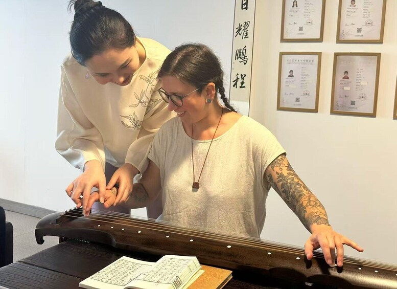 Two people playing a traditional stringed instrument, with sheet music on the table and certificates on the wall. 3