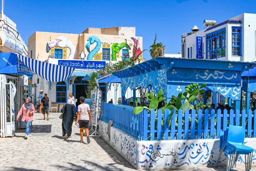 A street with blue and white buildings, a café named Café Zaraa, and a restaurant. 1