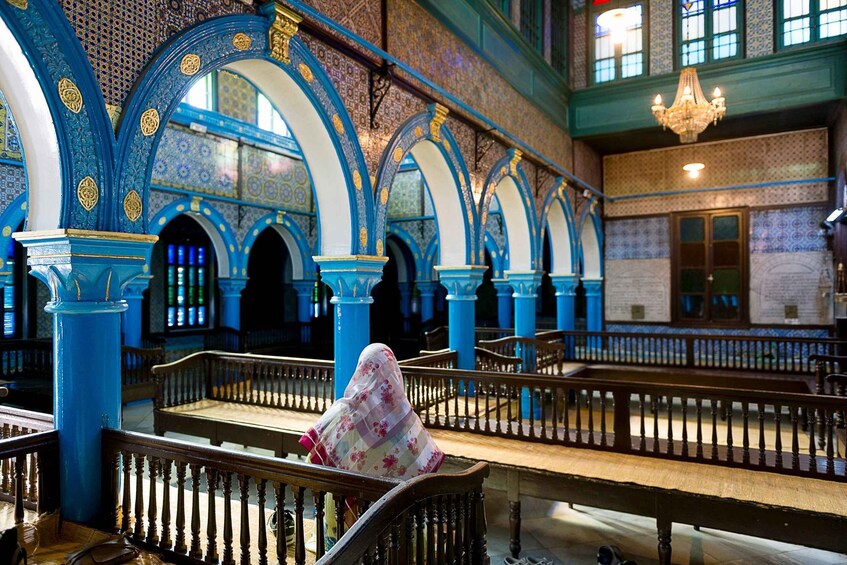 A person sitting on a bench in a room with blue and gold patterned walls and a chandelier. 3