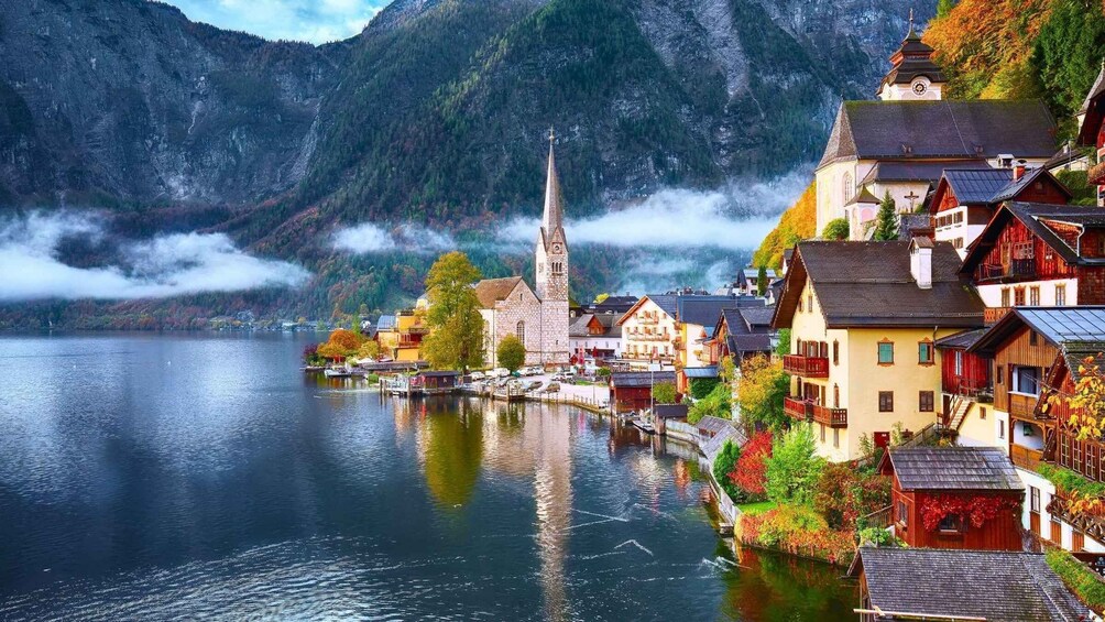 A lakeside village with traditional buildings, a church, and mountains in the background. 1