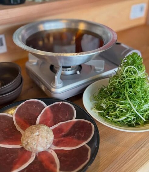 A hot pot setup with meat slices and a ball of meatball, surrounded by a bowl of greens. 5
