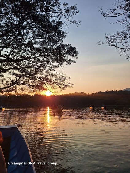 A sunset over a calm lake with boats and trees silhouetted against the sky. 1