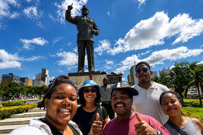 A group of people taking a selfie in front of a statue with a cityscape in the background. 1