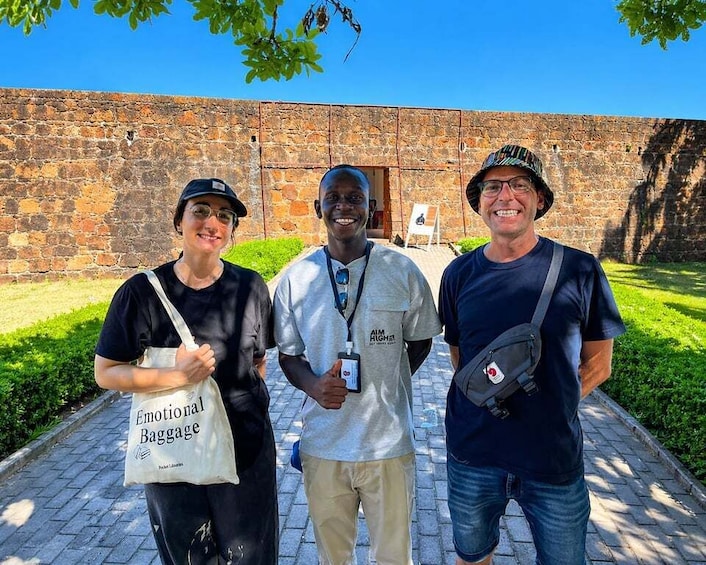 Three people standing in front of a stone wall with a grassy area and a paved walkway. 4