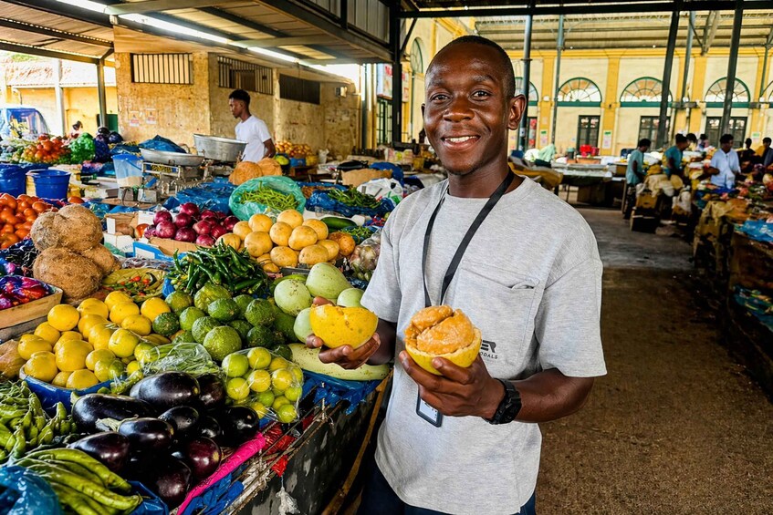 A person holding a fruit at a market with various vegetables and fruits displayed. 5