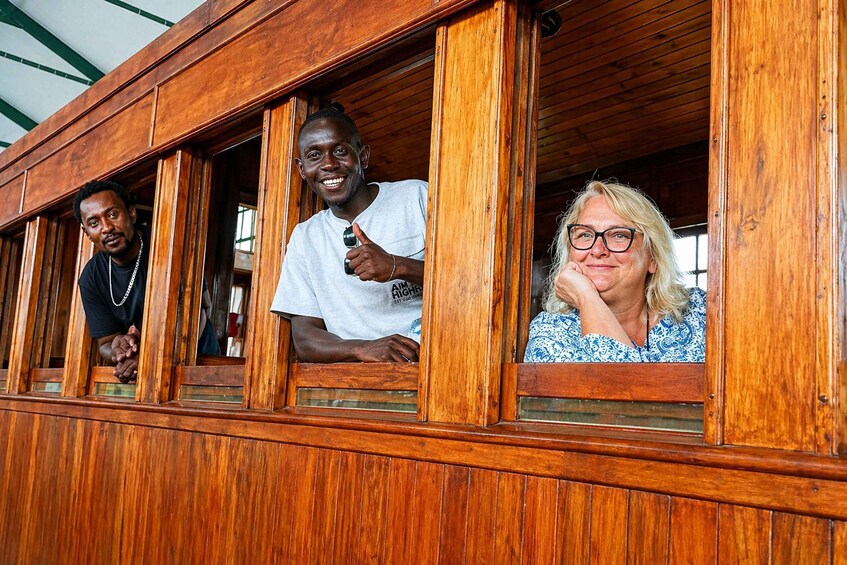 Three people seated in a wooden boat with windows. 3