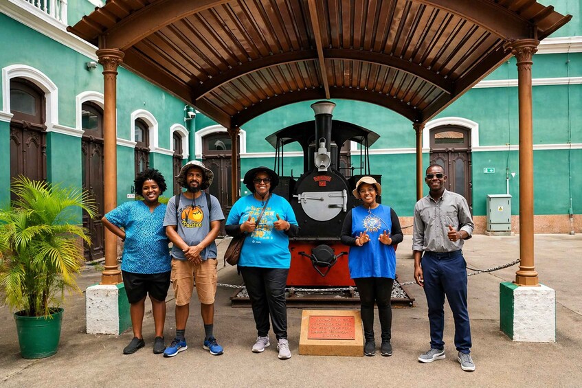 A group of people standing in front of a steam locomotive under a wooden shelter. 2