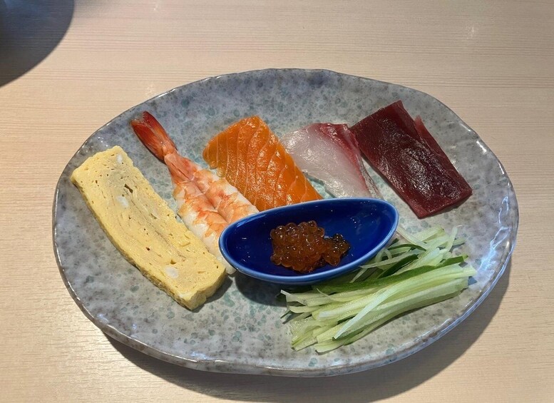 A plate of sashimi with various fish, a small bowl of roe, and some green vegetables. 1