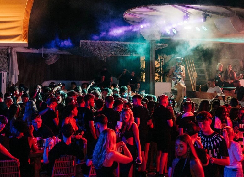 A crowded outdoor event with a stage and smoke effects. 1