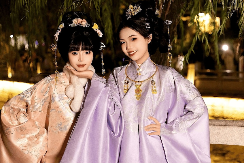 Two individuals in traditional attire with floral patterns and jewelry, standing outdoors at night. 5