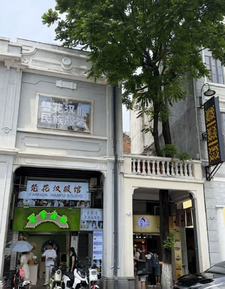 A building with signage in a foreign language, a tree in front, and a motorcycle parked outside. 4