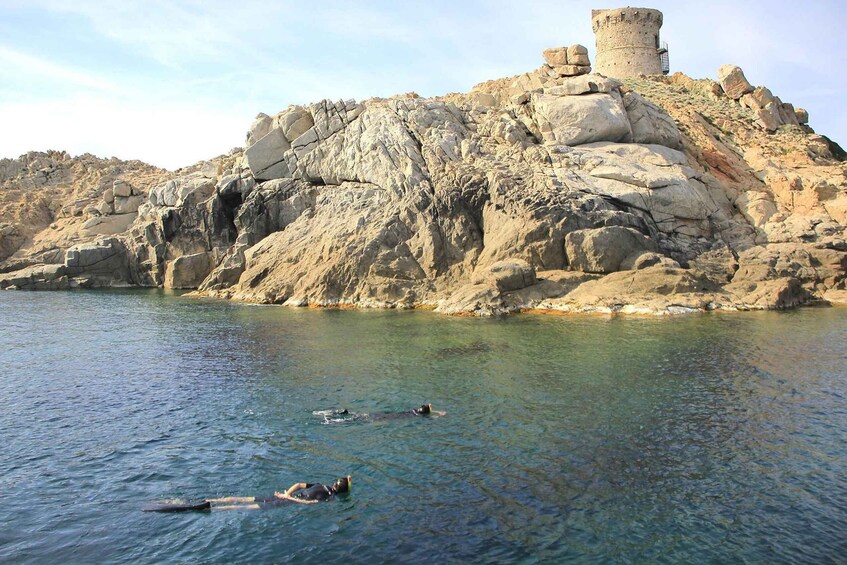 A rocky coastline with clear water, a tower, and people swimming. 3