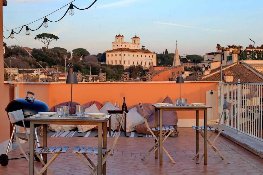 A rooftop terrace with tables and chairs, a grill, and a view of a historic building in the background. 5