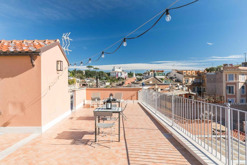 A rooftop terrace with a table and chairs, a string of lights, and a view of a coastal town. 2