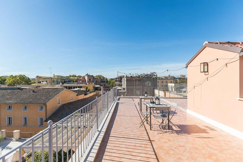 A rooftop terrace with a tiled floor, a metal railing, and a table with chairs. 3