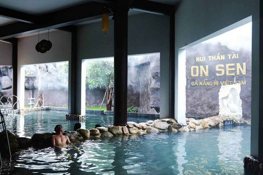 A hot spring with a person relaxing in the water, surrounded by rocks and a stone wall. 1
