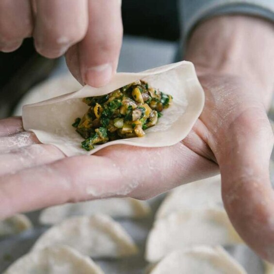 A person holding a dumpling with a filling of greens and possibly mushrooms. 3