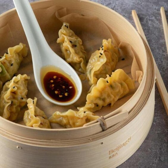 A bamboo steamer with dumplings and a dipping sauce. 2