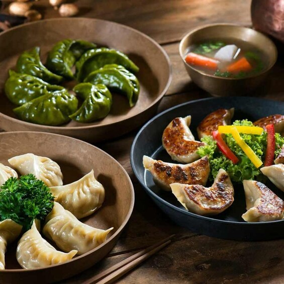 A variety of dumplings in different states of cooking, accompanied by a bowl of soup and fresh vegetables. 1