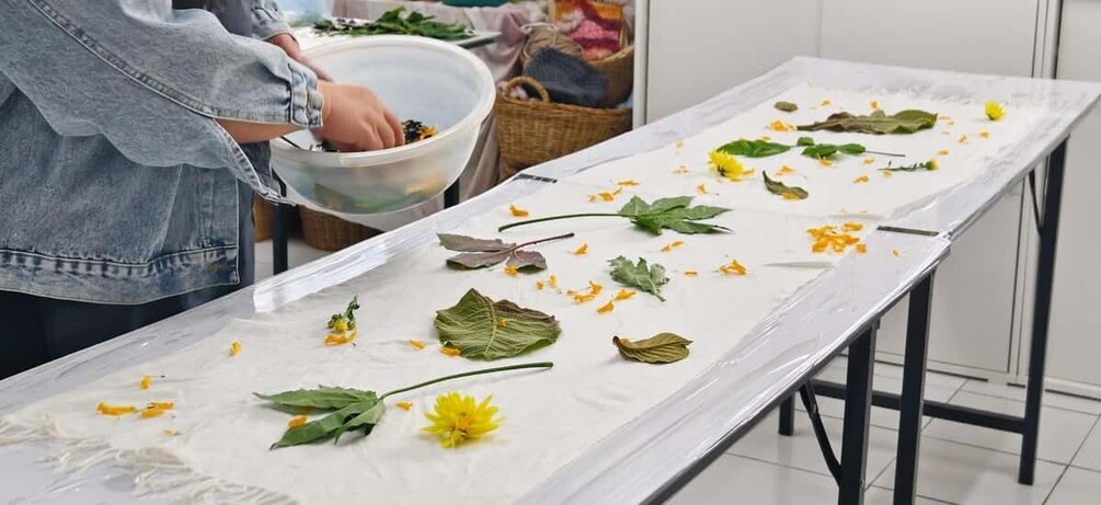 A person arranging leaves and flowers on a table. 4
