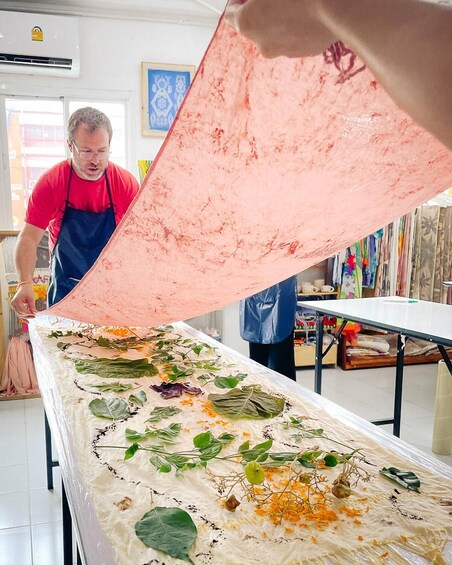 A person pouring a pink substance onto a table with leaves and orange flowers. 5