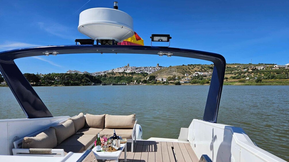 A boat with a white deck, beige cushions, and a table with drinks and flowers. 1