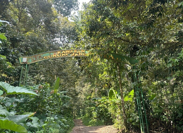 A signpost with 'Kawasan Gunung Jang' written on it, surrounded by dense tropical foliage. 2
