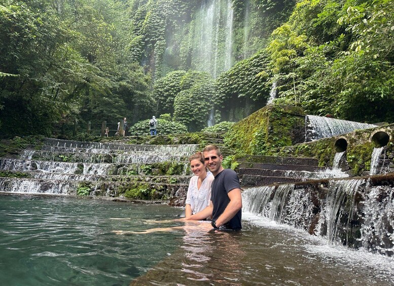 A couple standing in a waterfall pool surrounded by lush greenery. 1
