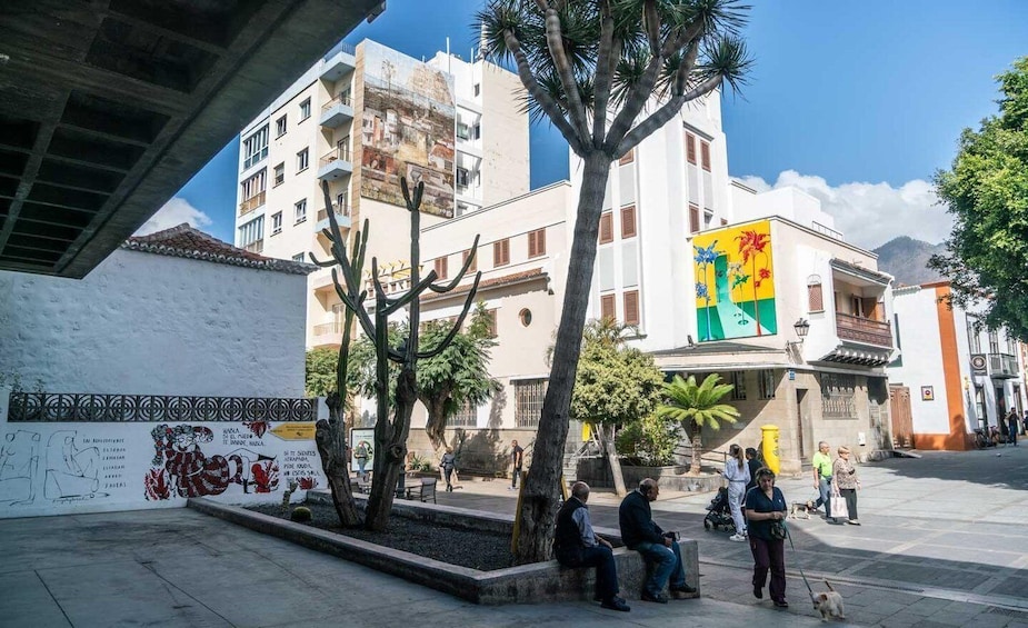 A plaza with people walking, a mural, and a building with a colorful sign. 3