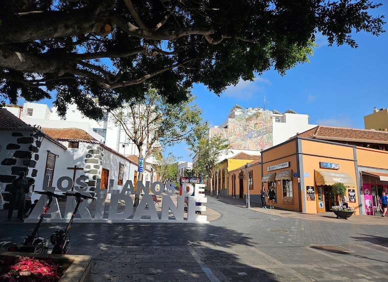 A street with buildings, a cross, and a sign that reads 'LOS LANOS DE HERRANDE.' 1