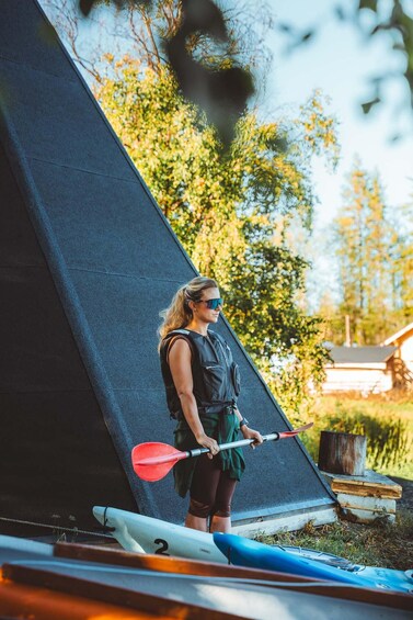 A person standing next to a kayak, holding a paddle, with a tent and trees in the background. 5