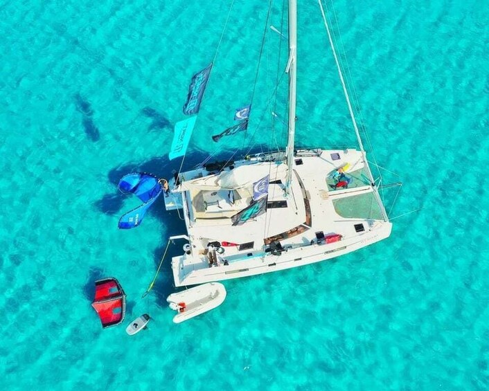 A sailboat anchored in clear turquoise waters with a smaller boat nearby. 1