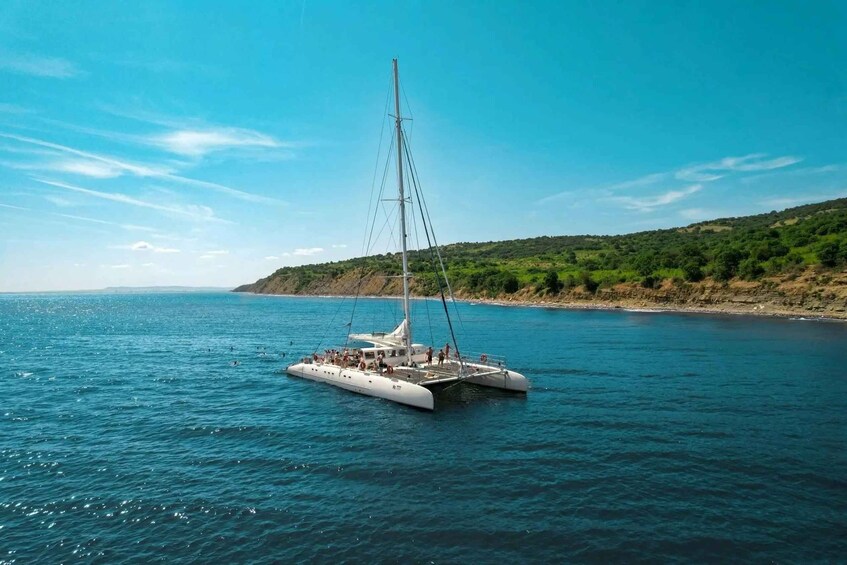A white catamaran on calm blue waters with a clear sky and a hilly coastline in the background. 3