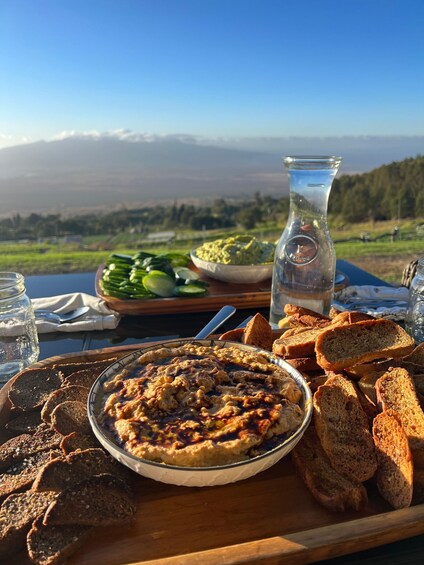 A meal with hummus, bread, and vegetables on a table with a scenic mountain view. 1