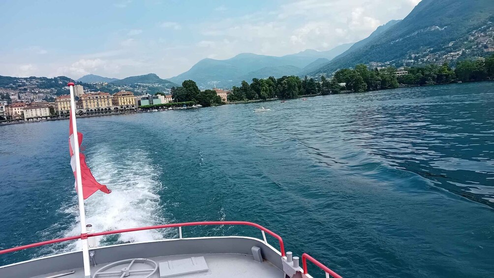 A boat moving through a lake with a cityscape and mountains in the background. 3
